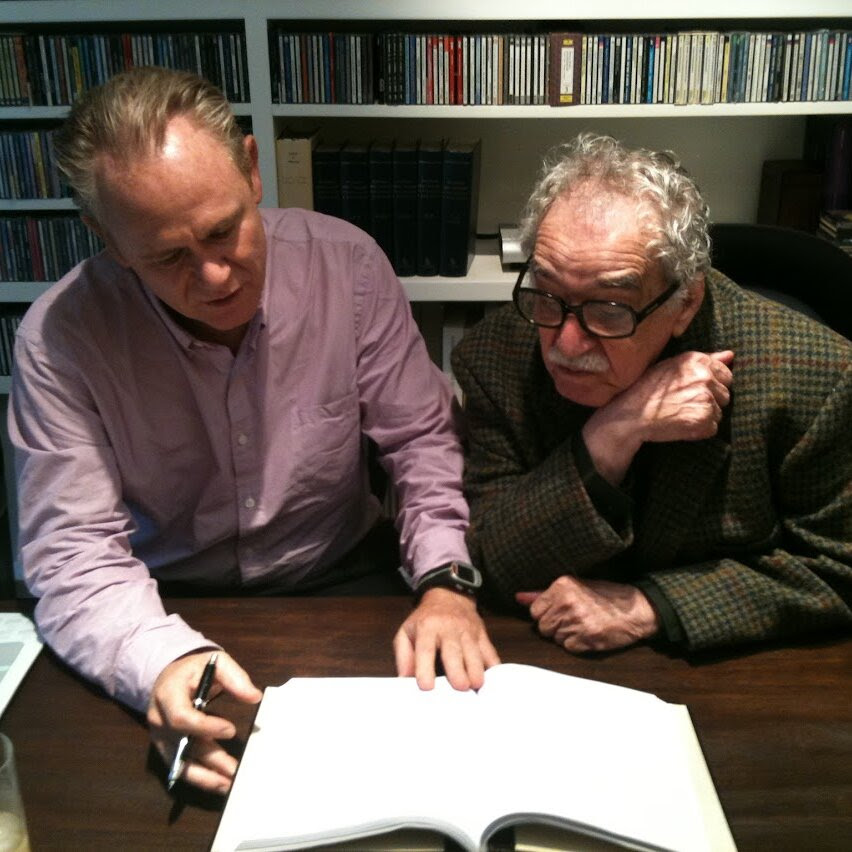 Editor Cristóbal Pera and author Gabriel García Márquez lean over a manuscript together. Behind them are shelves with what look like CDs. 