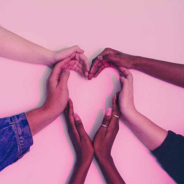 Close-up of six human hands with diverse skin tones forming the shape of a heart together with a light pink background