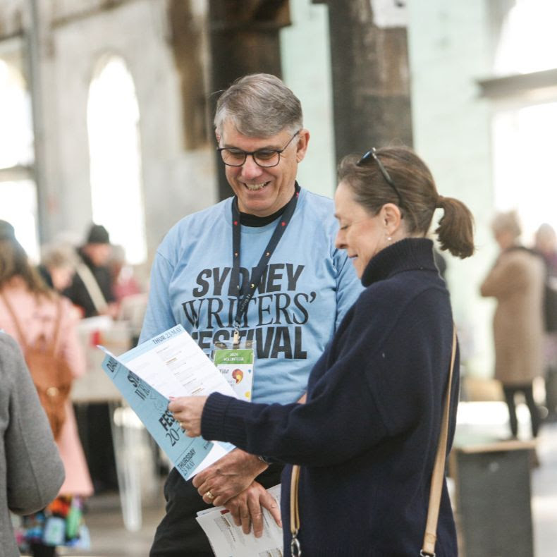 A volunteer in blue shirt helps an audience member in a turtleneck jumper