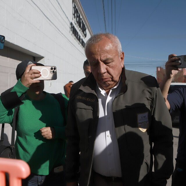 An older, gray-haired man walks amid a crowd of people pointing cellphones at him.