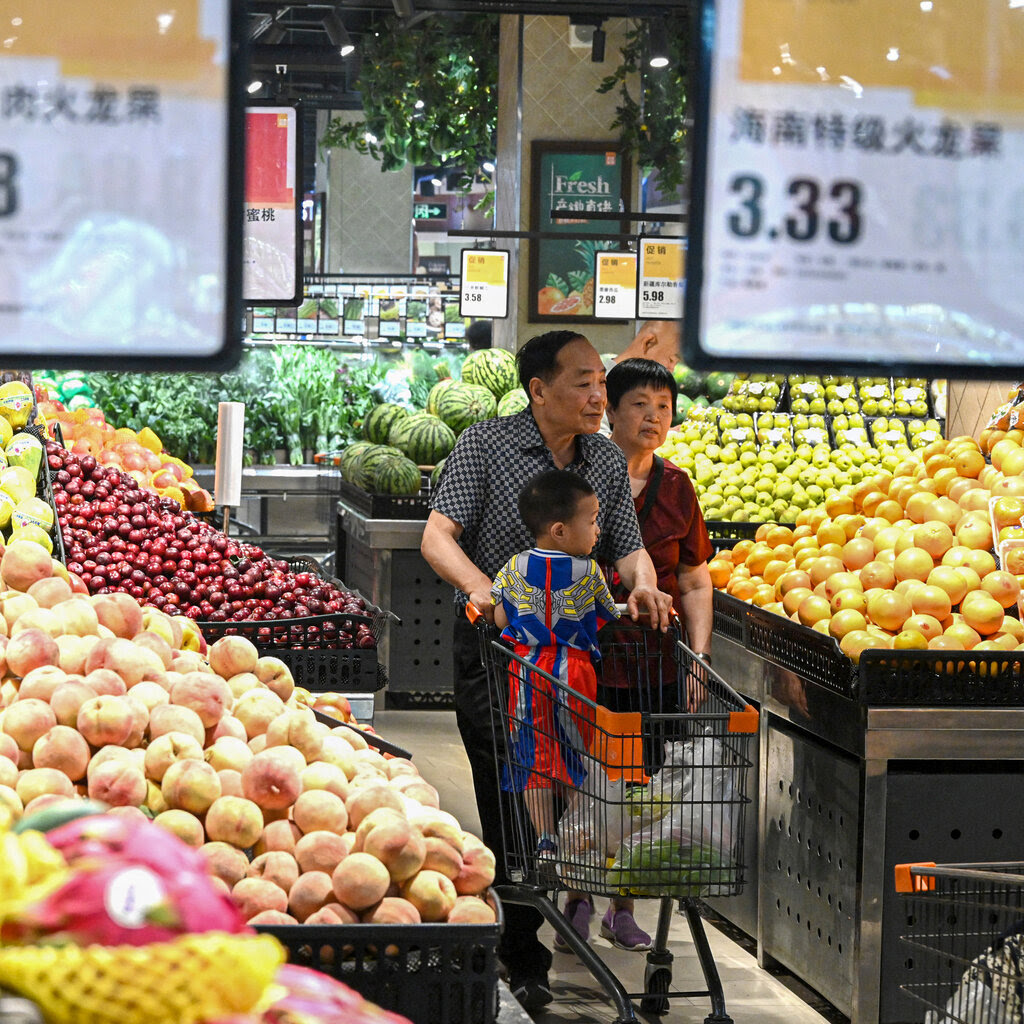 People walking through a grocery store browsing the fruit and vegetables, with a child in a shopping cart. 