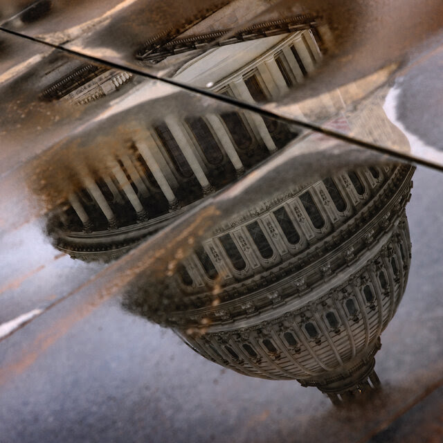 The dome of the U.S. Capitol, reflected in puddles on pavement.