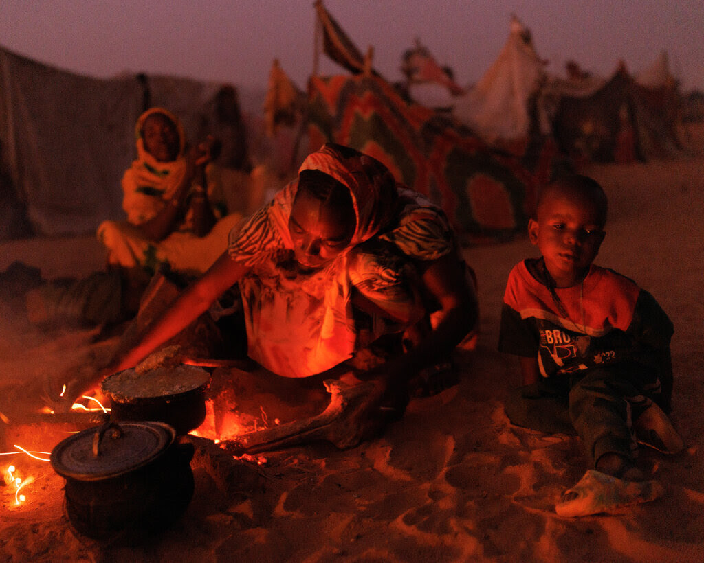 Sudanese refugees cook food over a fire outside their makeshift shelters.