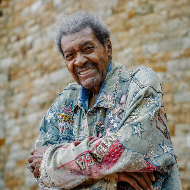 Don King posing in a denim jacket decorated in rhinestones, American flags, stars and stripes. 