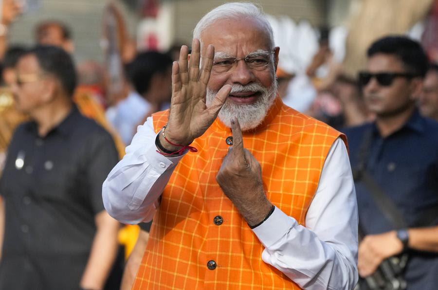 Indian Prime Minister Narendra Modi waves with one hand and holds up his other hand to show the ink mark on his finger after casting his vote in the election.
