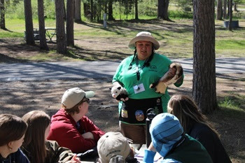 Falechia Barry, explorer guide at Interlochen State Park, shows animal furs to a group of kids and parents gathered in a forest area
