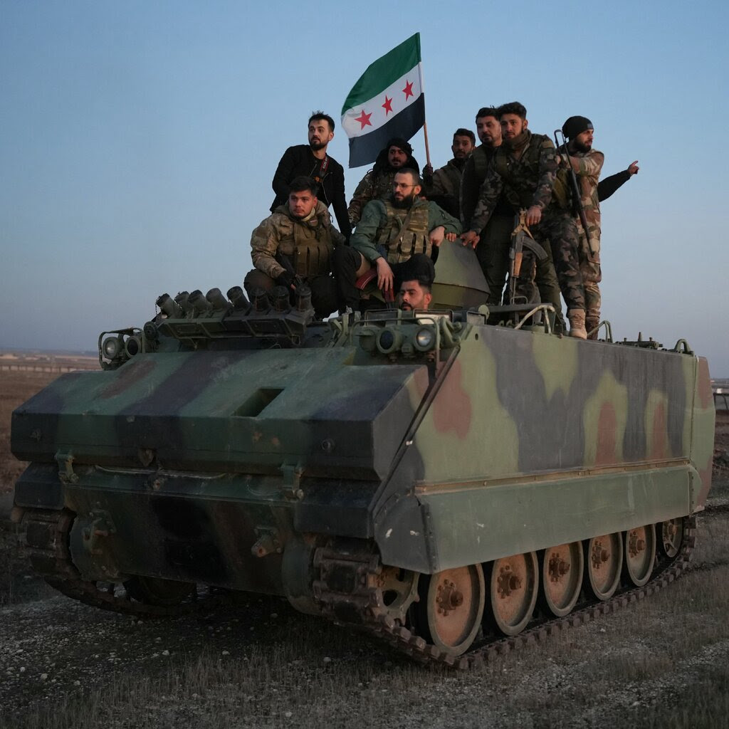 Fighters atop a tank with a flag of green, white and black bands and red stars. 