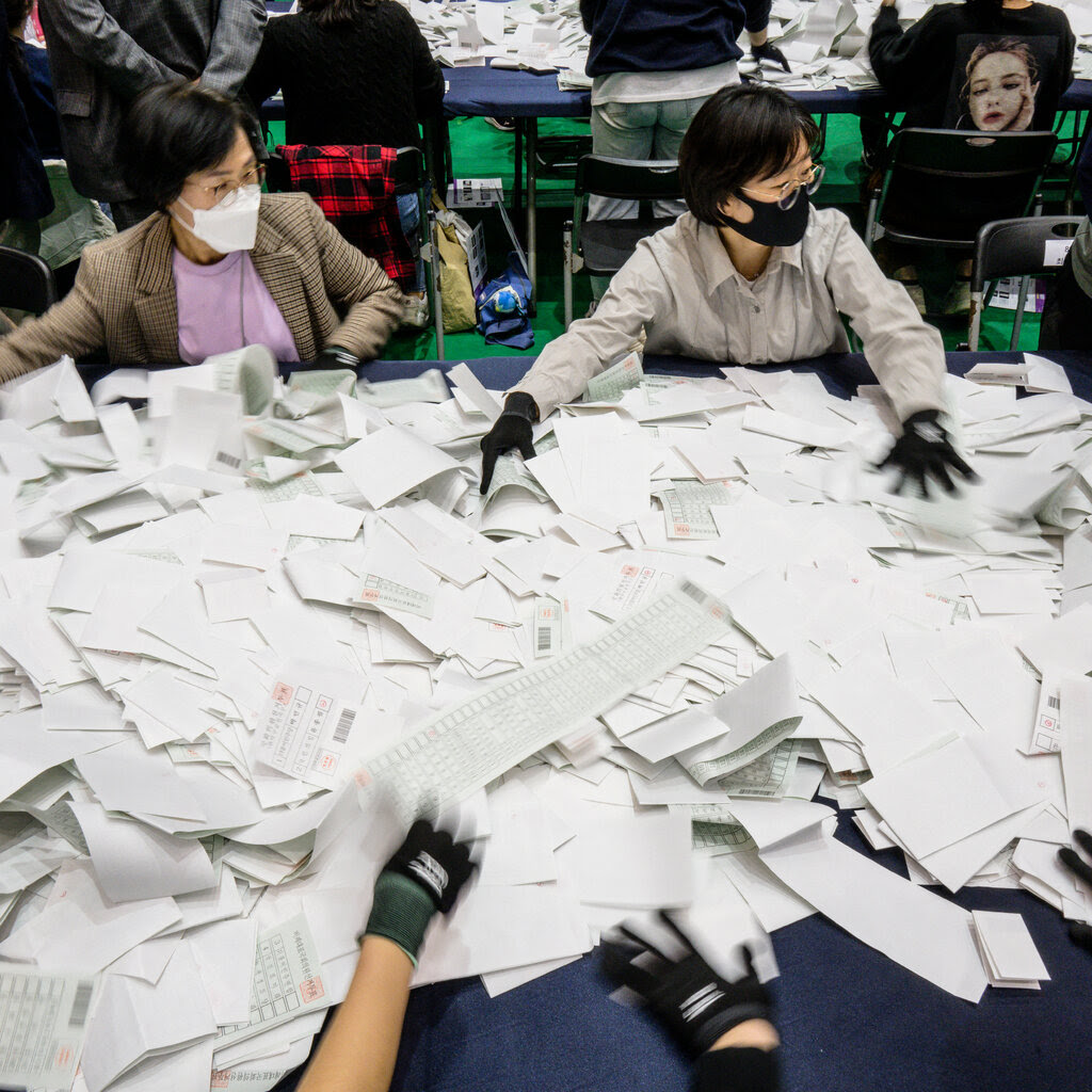 People wearing masks and gloves sift through pieces of paper. 