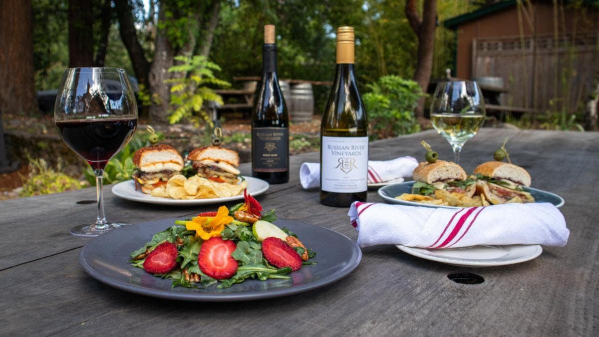 table with bottle of wine, wine glass, and plate of sandwiches