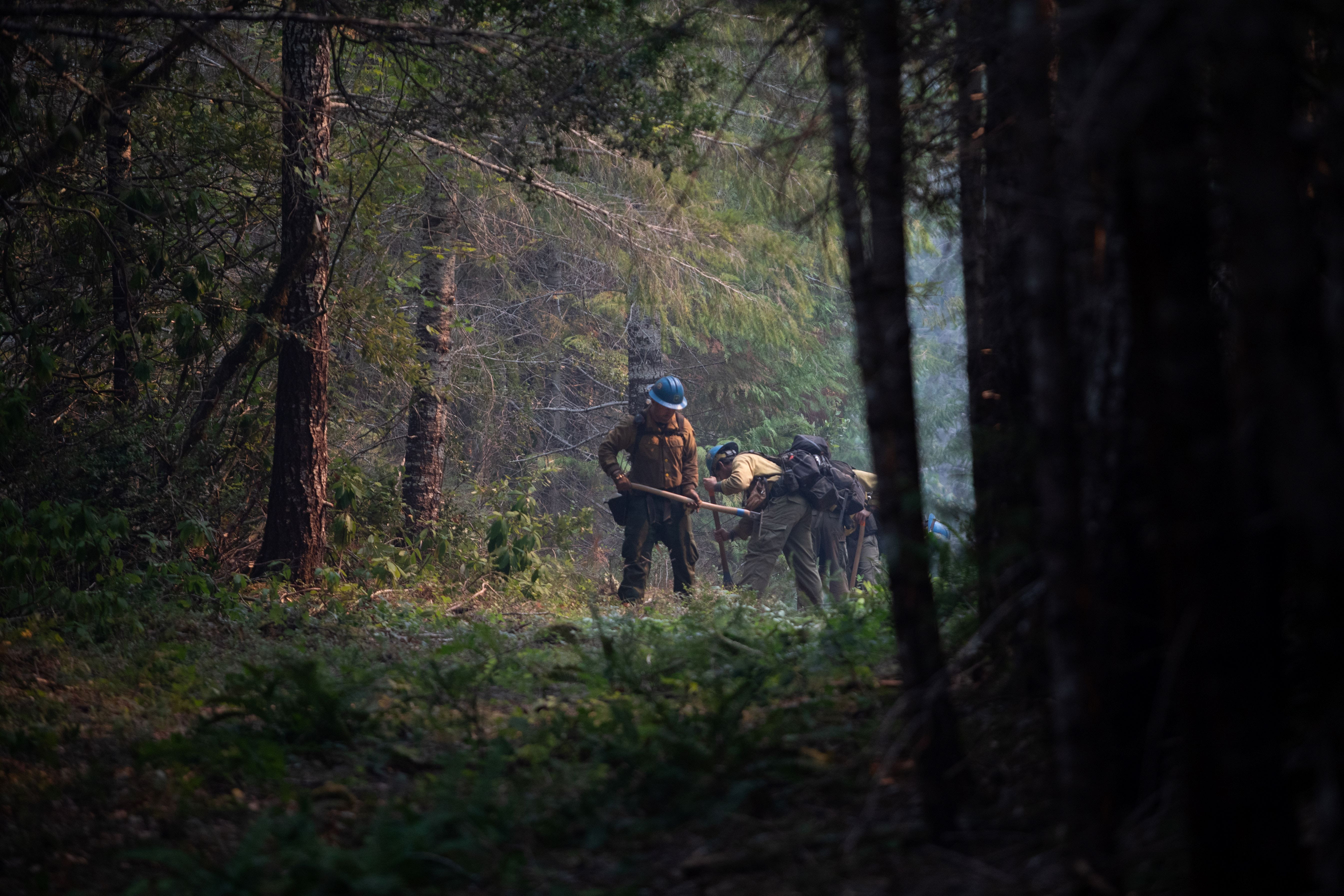 Firefighters use pickaxes clearing between trees.