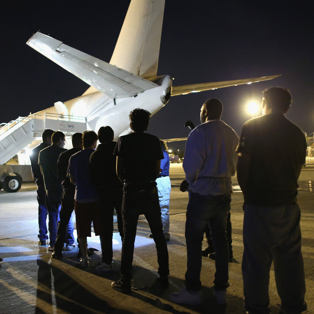 A queue of men stand in front of a jet. 