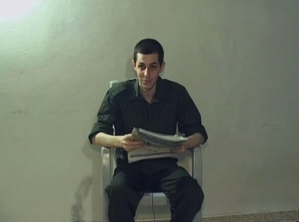 Une capture d'écran d'une vidéo montre Gilad Shalit assis et tenant un journal.