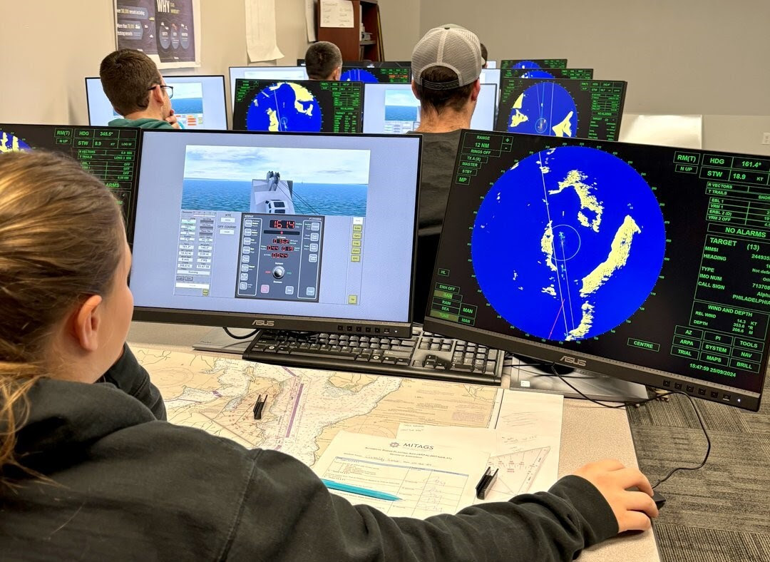 Students in a classroom use monitors displaying a navigational simulation and radar charts