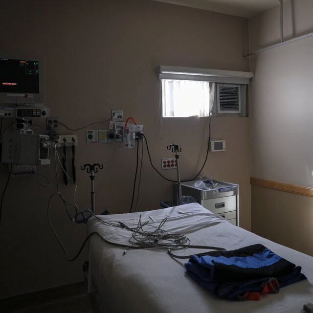 An empty hospital bed in a hospital with medical equipment and a drawn curtain nearby.