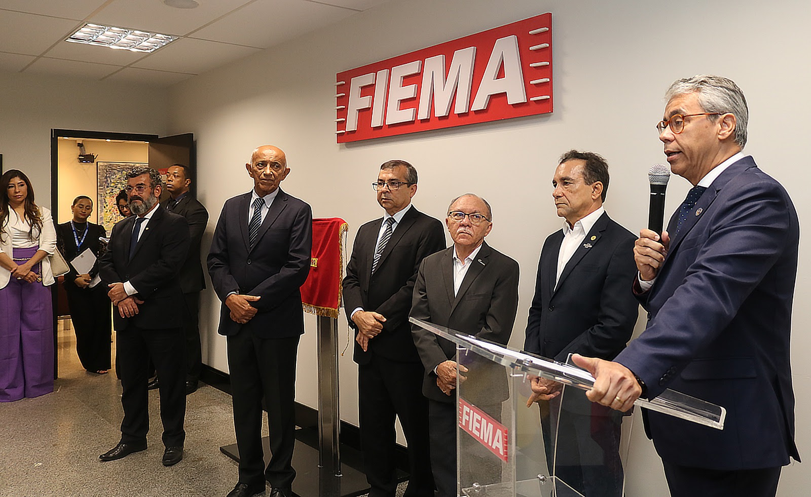 Foto colorida mostra autoridades em pé, homens e mulheres, durante solenidade de inauguração do 2º Centro de Mediação e Conciliação de São Luís, na FIEMA. Na foto o presidente do TJMA, desembargador Paulo Velten, fala ao microfone.