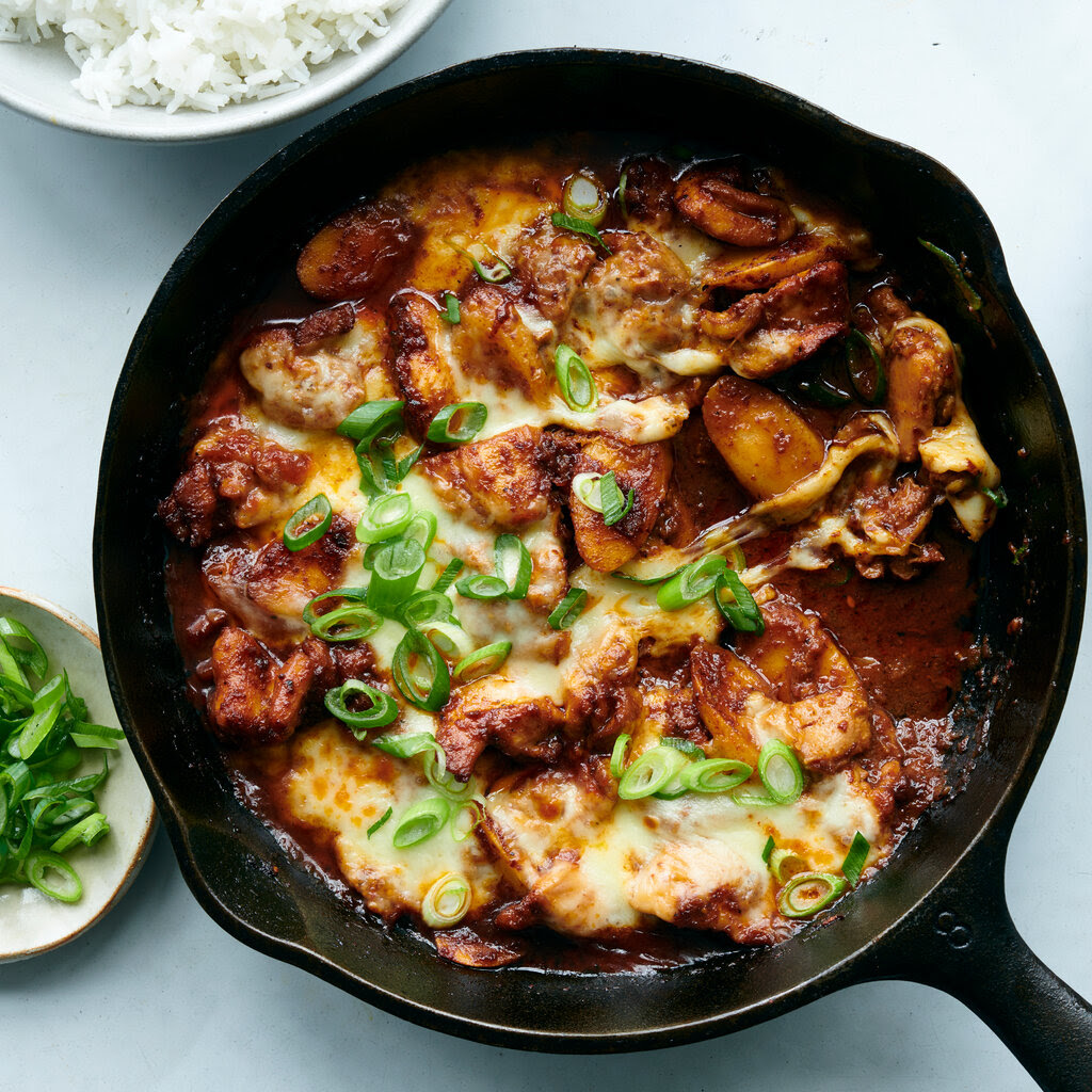 A skillet of cheesy chicken topped with scallions. 