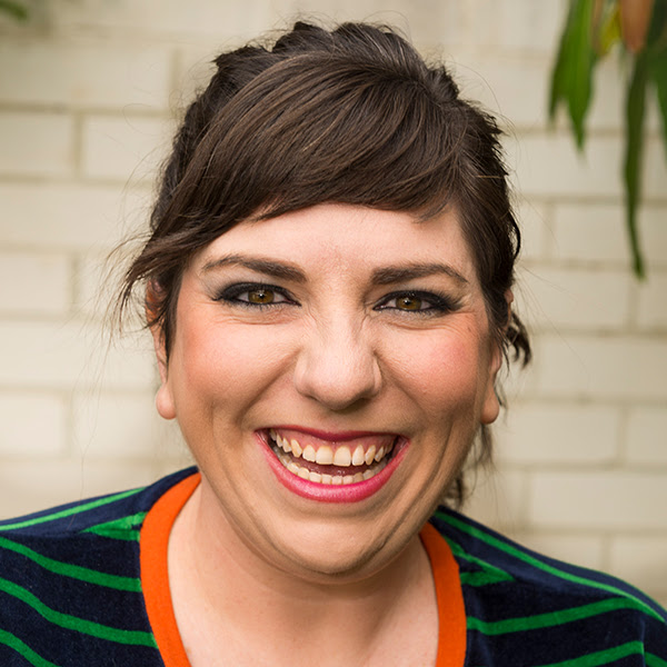 A woman in front of a brick wall smiling widely