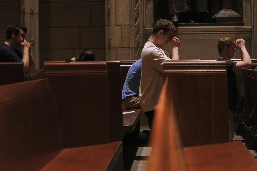 People kneel in wooden pews in a Catholic church.