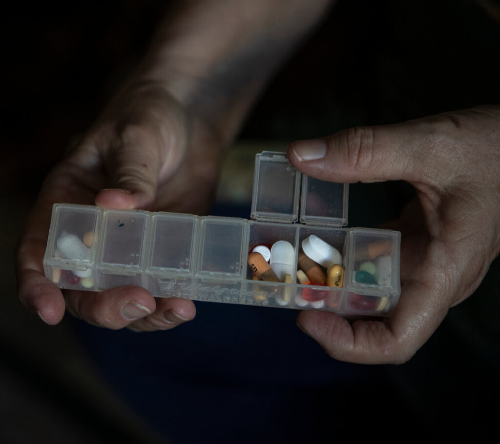 A pair of hands holds a weekly medication organizer filled with pills. 