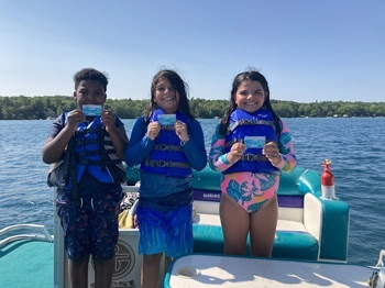 Three children properly wearing life jackets stand on a boat, proudly displaying newly-won McDonald's certificates.