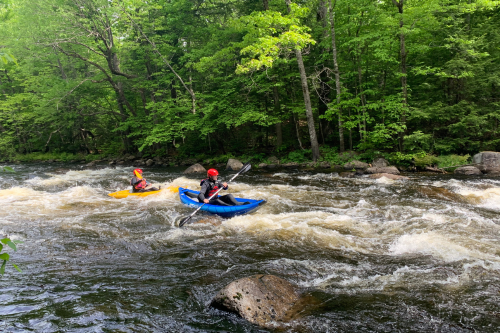 Two kayaks in a whitewater stream in the forest.