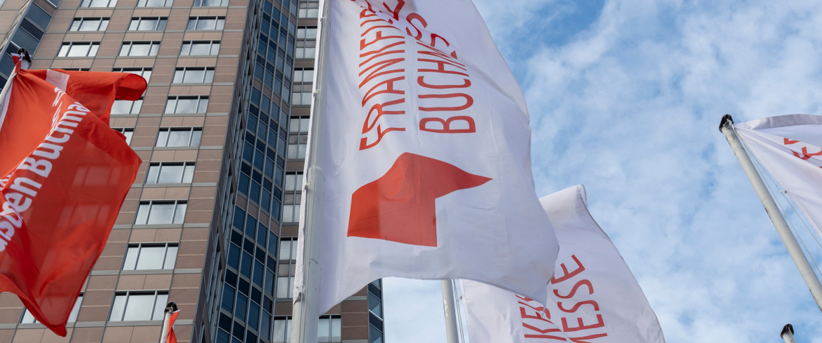 Frankfurter Buchmesse red and white flags against a blue sky with clouds and a skyscraper.