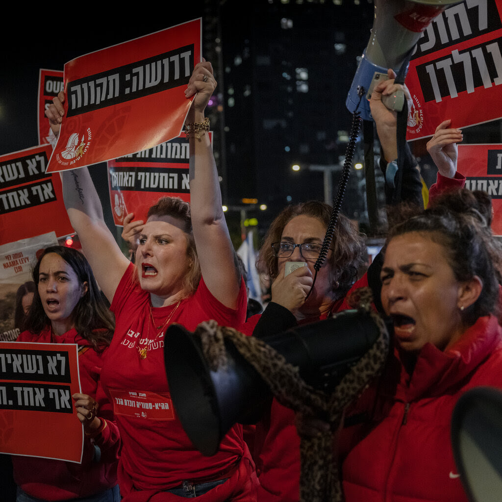 People wearing red hold up posters and shout.