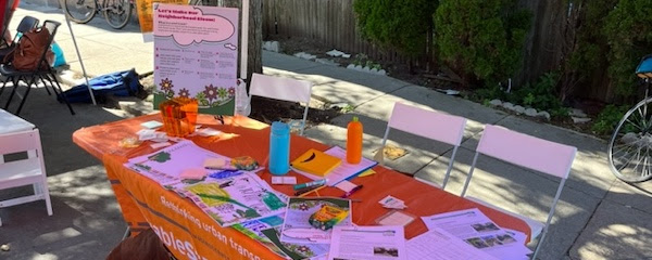 a table at last year's open streets event,
with an orange tablecloth with the livablestreets logo. the table is
covered in papers with information about local greenway projects, and
next to the table is a large posterboard with an interactive activity