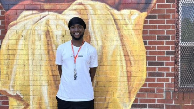 A man standing infront of a mural and smiling at beasley Community Centre