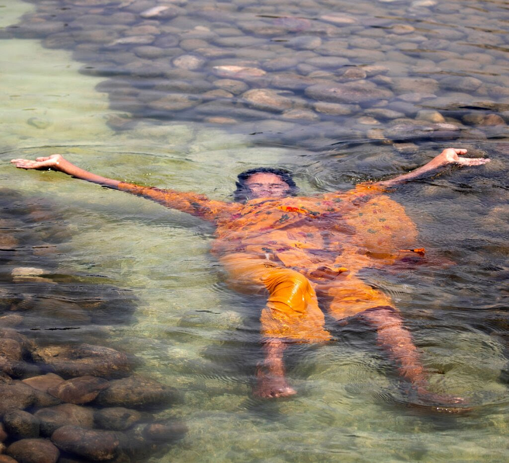 A girl dressed in an orange sari lies in water with her arms outstretched. 