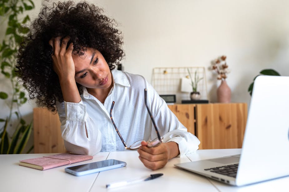 An exhausted-looking woman stares forlornly at her laptop screen.