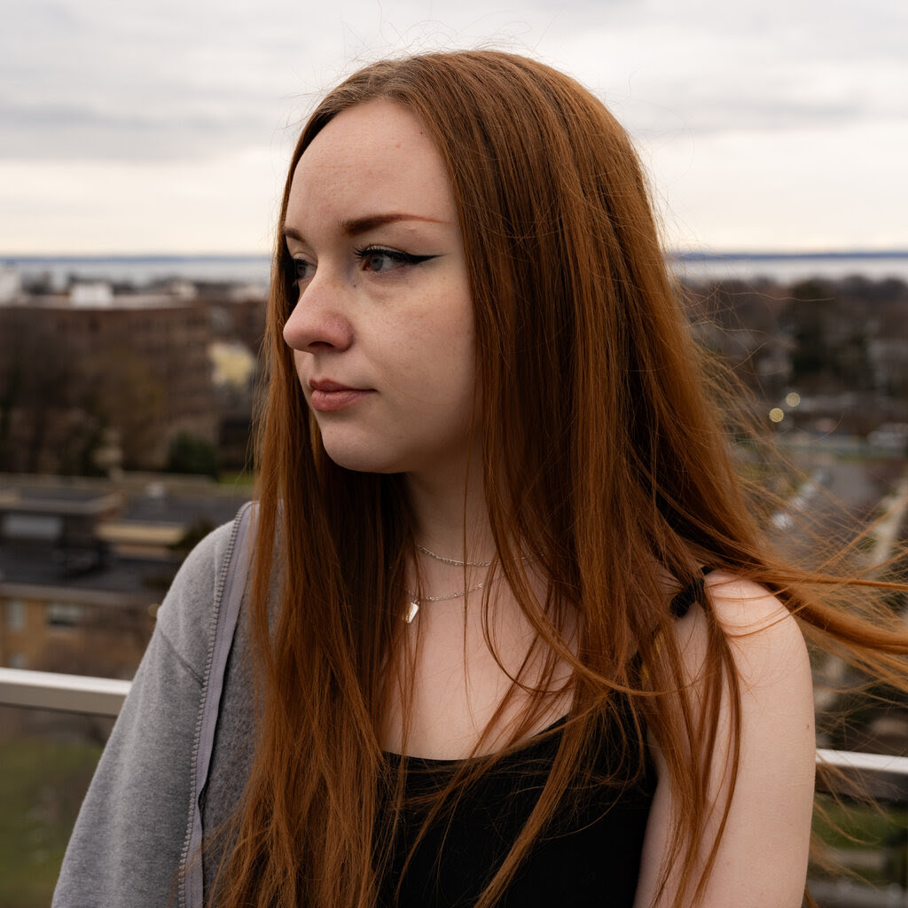 A person with long red hair looks to the side. 