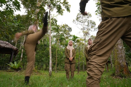 Three women in khaki uniforms watch as another does a high taekwondo kick