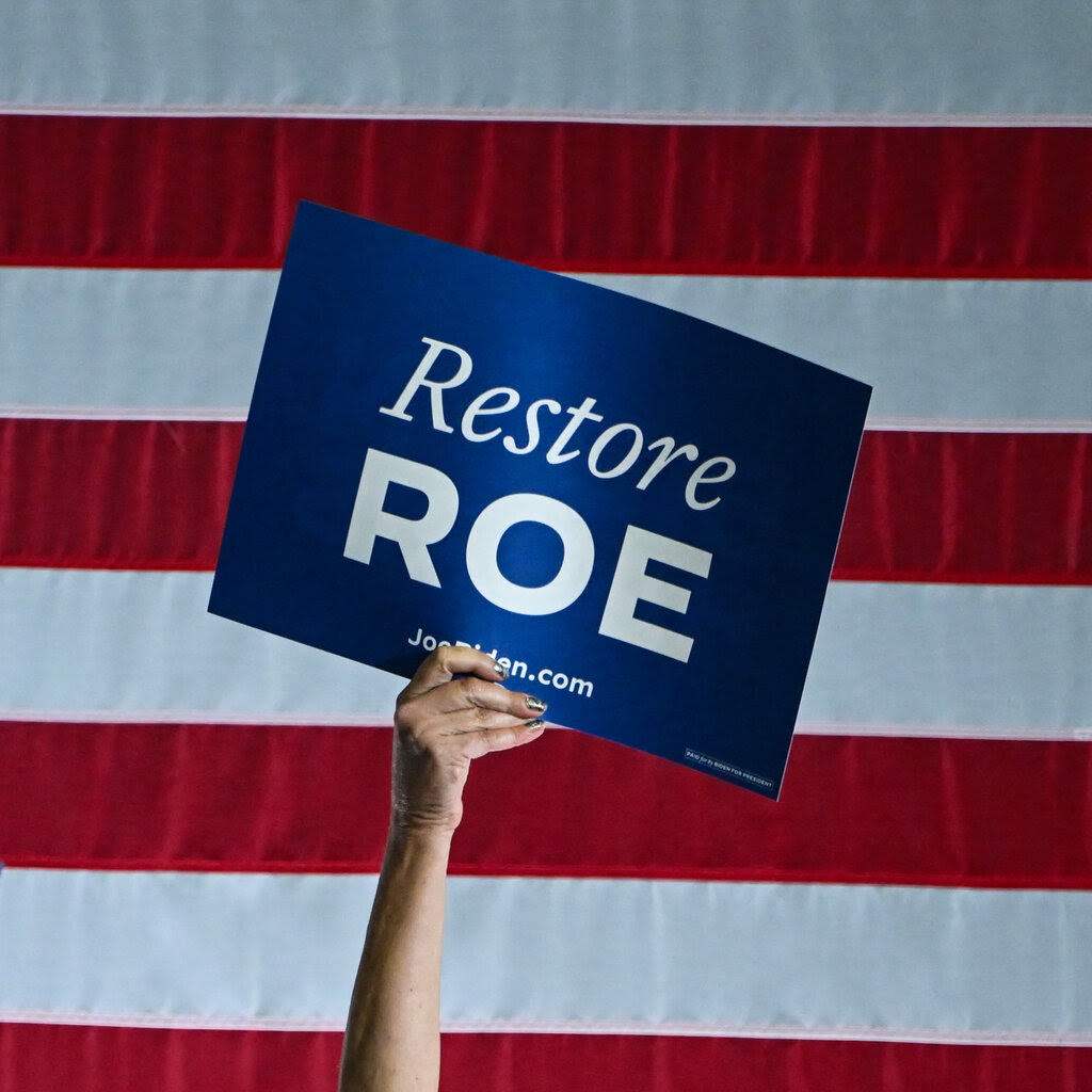 A hand raising a Biden campaign sign that reads “Restore Roe.”