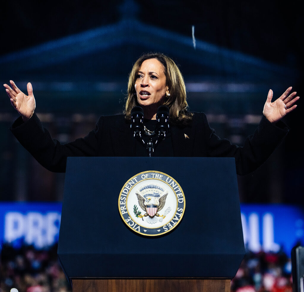 Kamala Harris speaks at a lectern arms outstretched. 