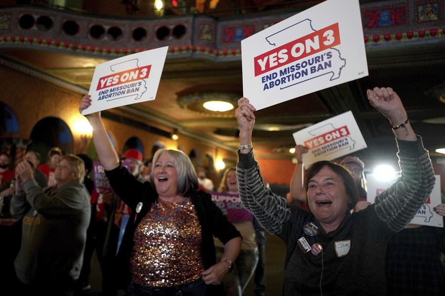 Women holding signs that say "YES ON 3 END MISSOURI'S ABORTION BAN" raise their signs and celebrate.