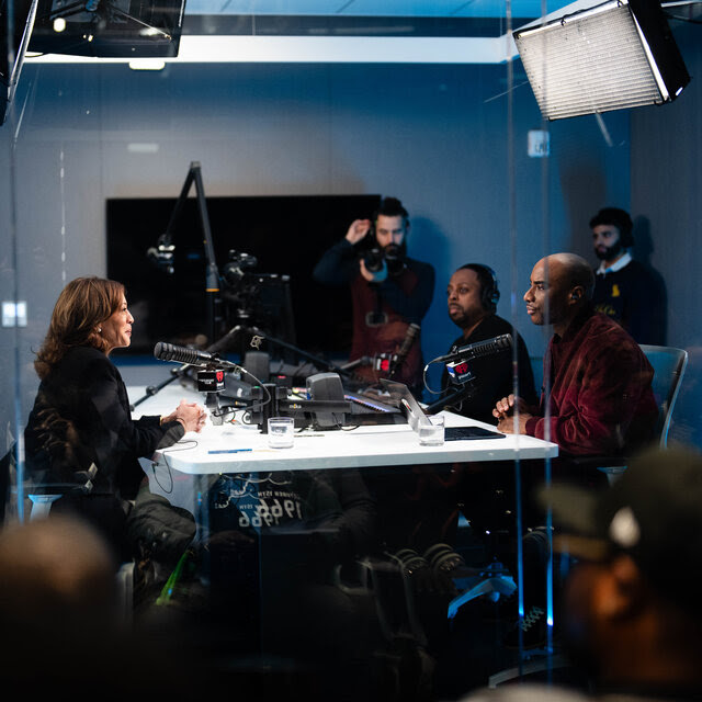 Kamala Harris in a recording studio, sitting opposite Charlamagne Tha God as they speak into microphones.