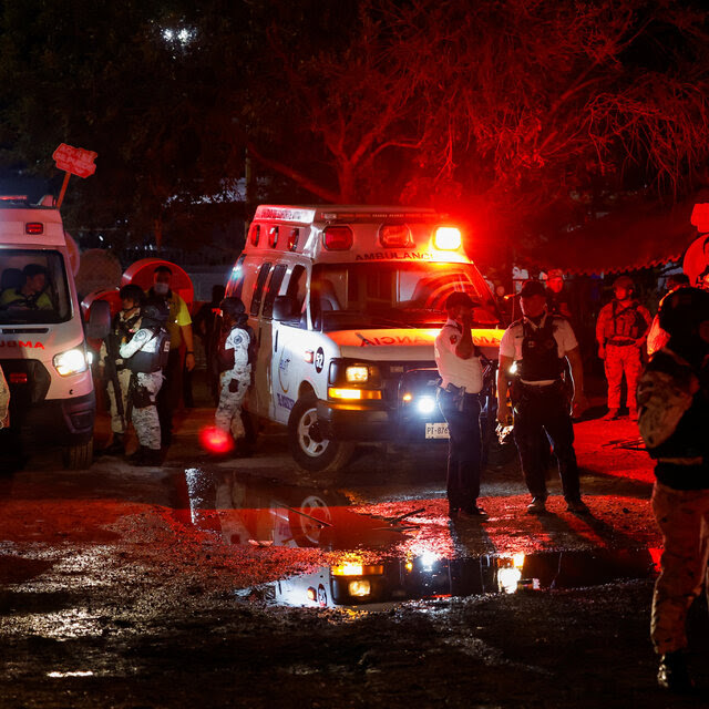 Emergency workers stand near ambulances in the dark. 