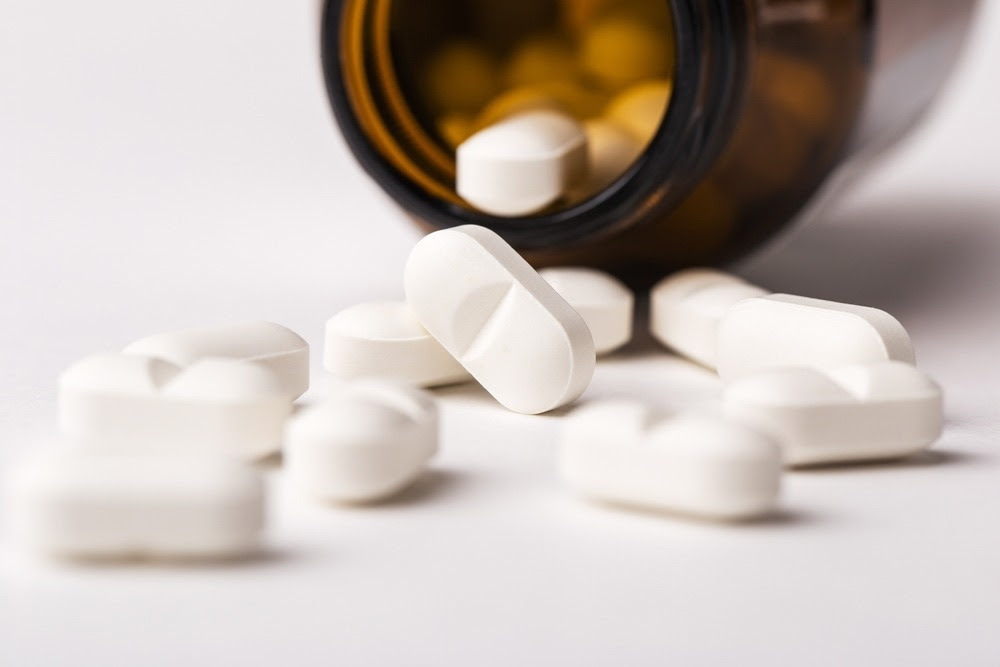 Close up magnesium supplements fell out of a glass bottle on a white background. Image Credit: Gala Oleksenko/Shutterstock.com