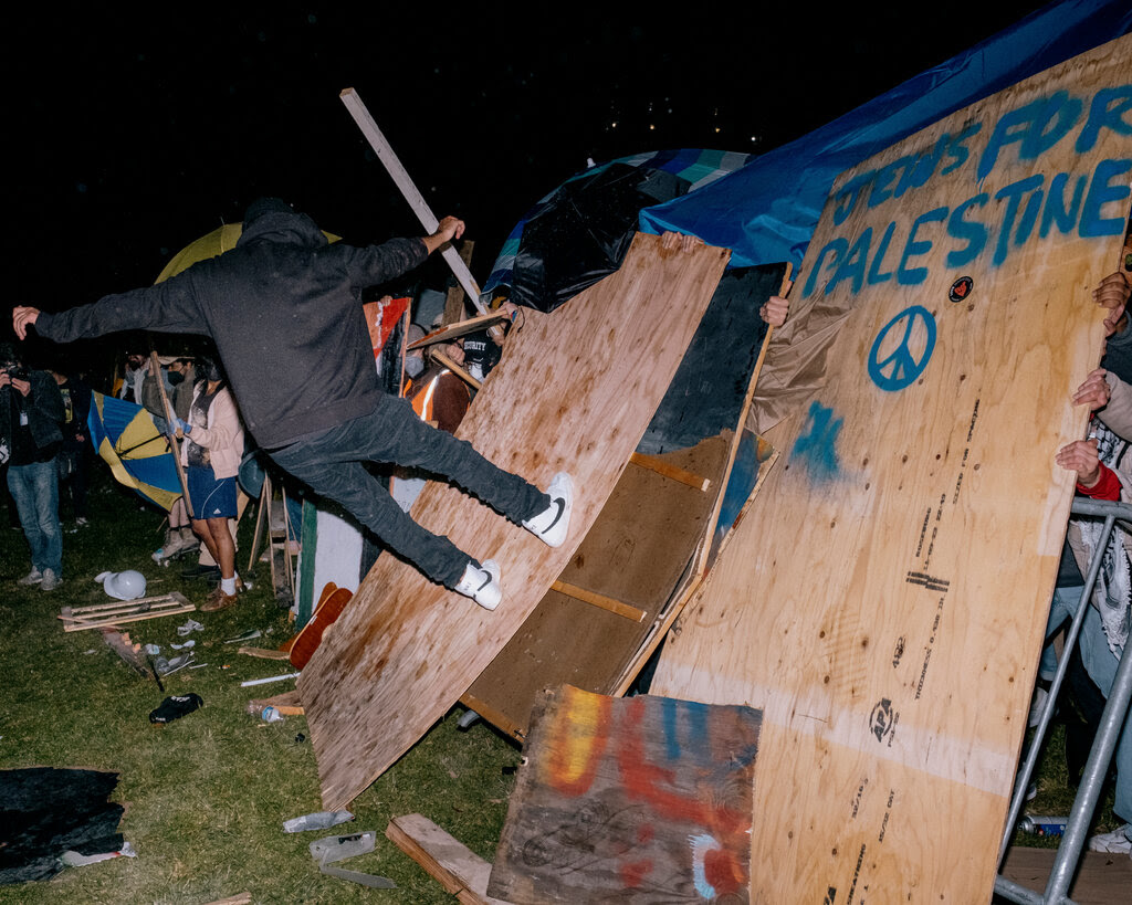 A counterprotester leaps into a plywood barricade at a pro-Palestine encampment.