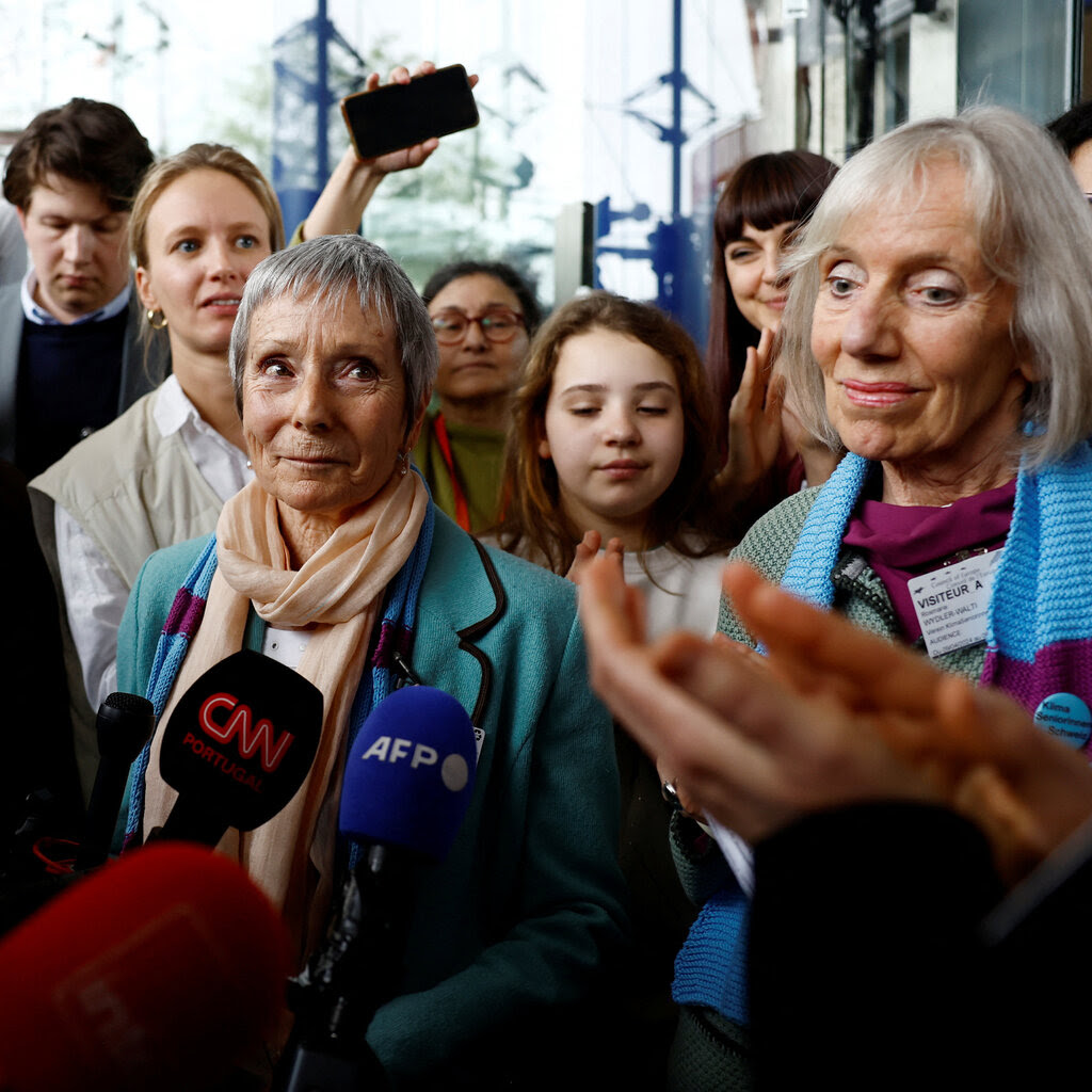 A group of older women stand smiling in front of CNN and AFP microphones. 