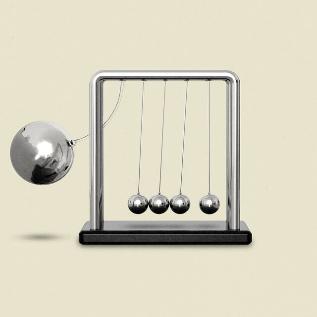 A Newton’s cradle device of five metals balls, with a larger one to the left about to slam into the others.