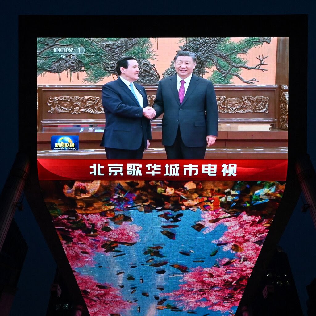 A television shows two men shaking hands, with Chinese lettering at the bottom. 