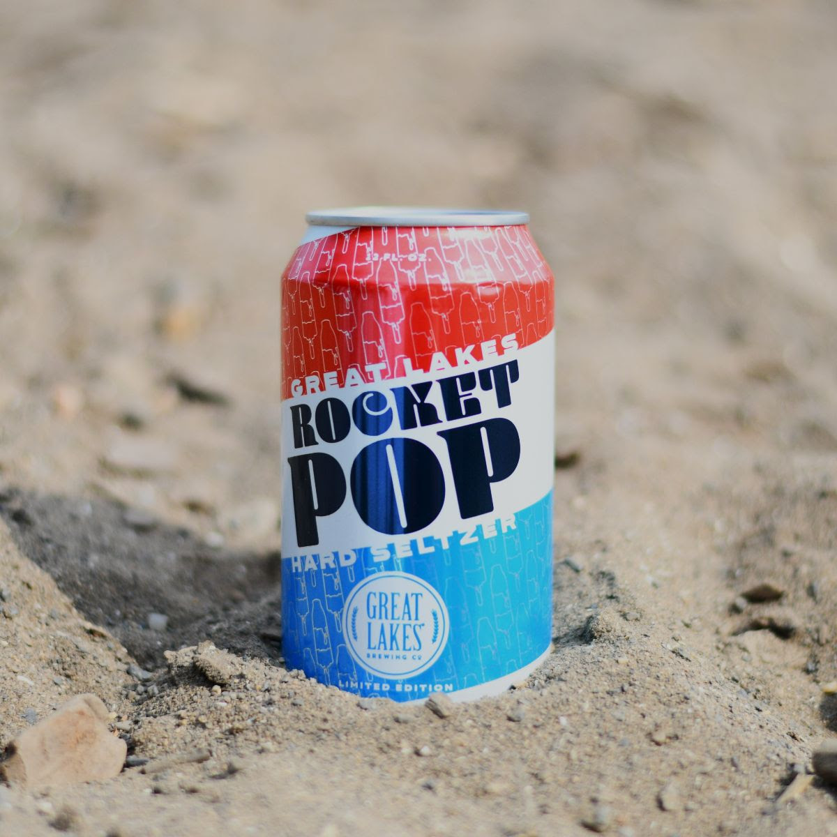 12 oz. Can Rocket Pop Hard Seltzer slightly buried in a sandy beach.