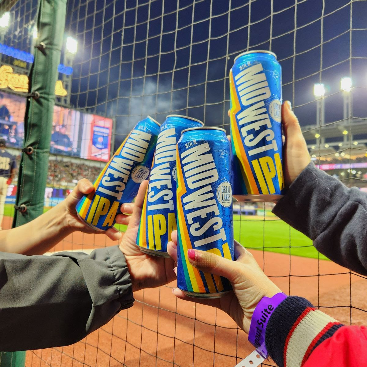 Close up of four people toasting with 19.2 oz. Cans of Midwest IPA from a dugout suite at the Cleveland baseball stadium.