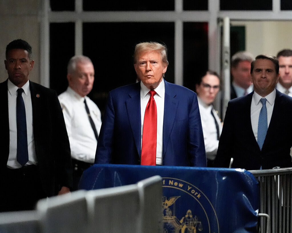 Donald Trump in a courtroom hallway amid security officers.
