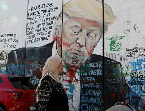 A Palestinian woman walks past a mural depicting former U.S. President Donald Trump in Bethlehem, West Bank, Tuesday.