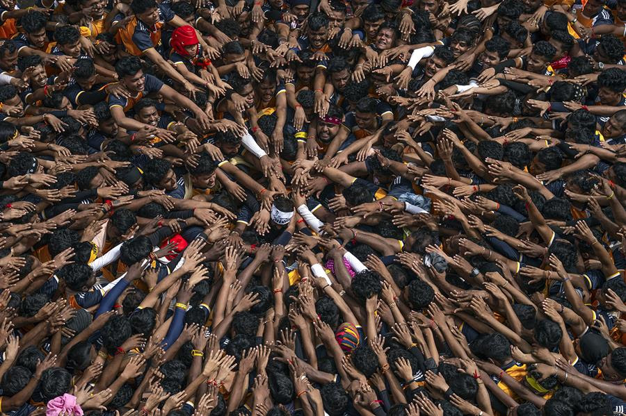 A crowd of people lay hands towards a single individual at the center of the group.