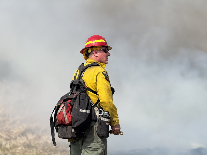 Ranger wearing fire gear at prescribed fire site as smoke fills the air behind him