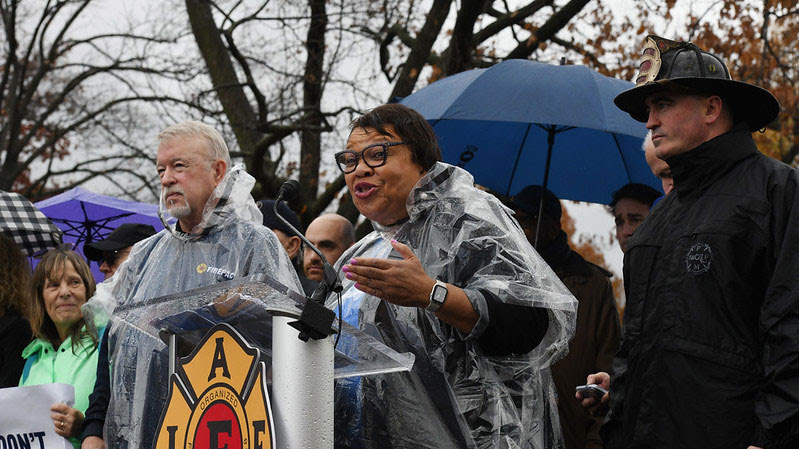 Princess Moss wears a poncho and speaks at a podium in the rain.